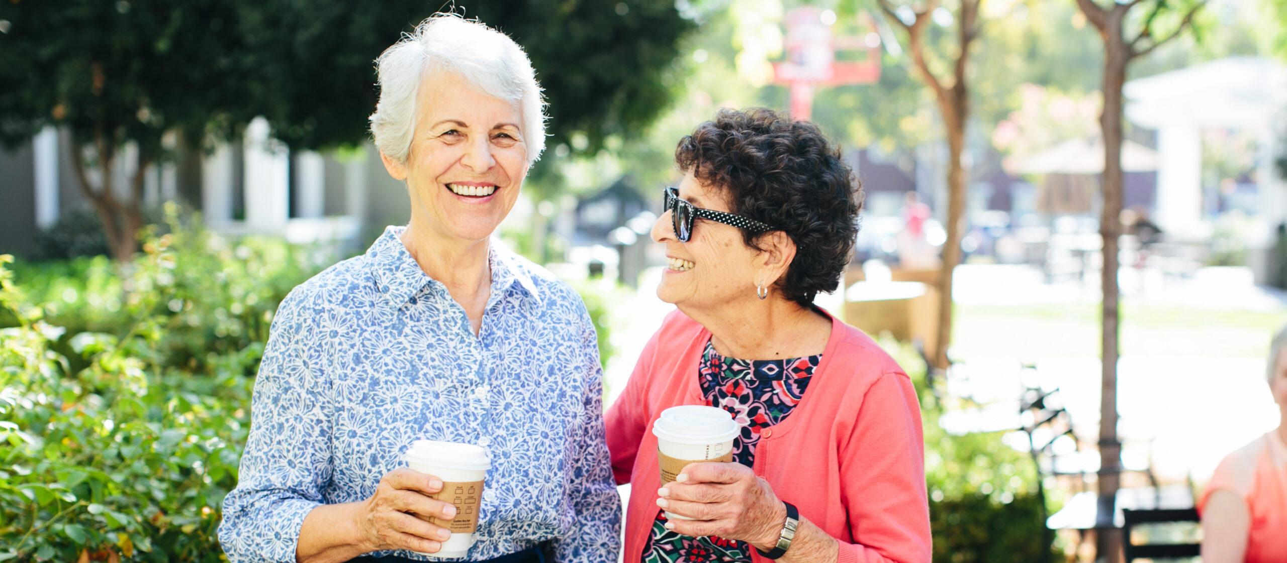Two smiling women enjoy coffee outdoors