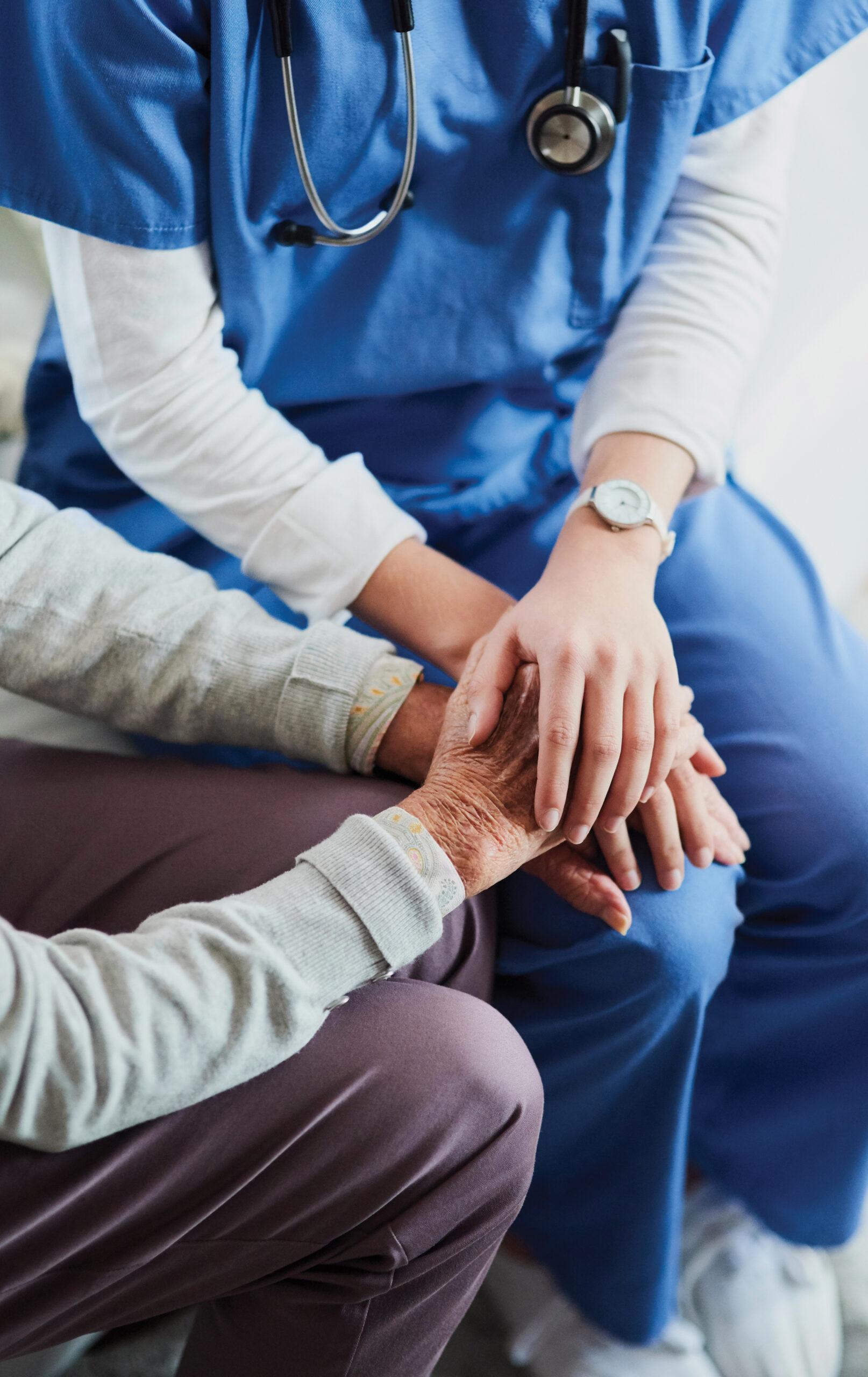 A nurse compassionately holds a patient's hands