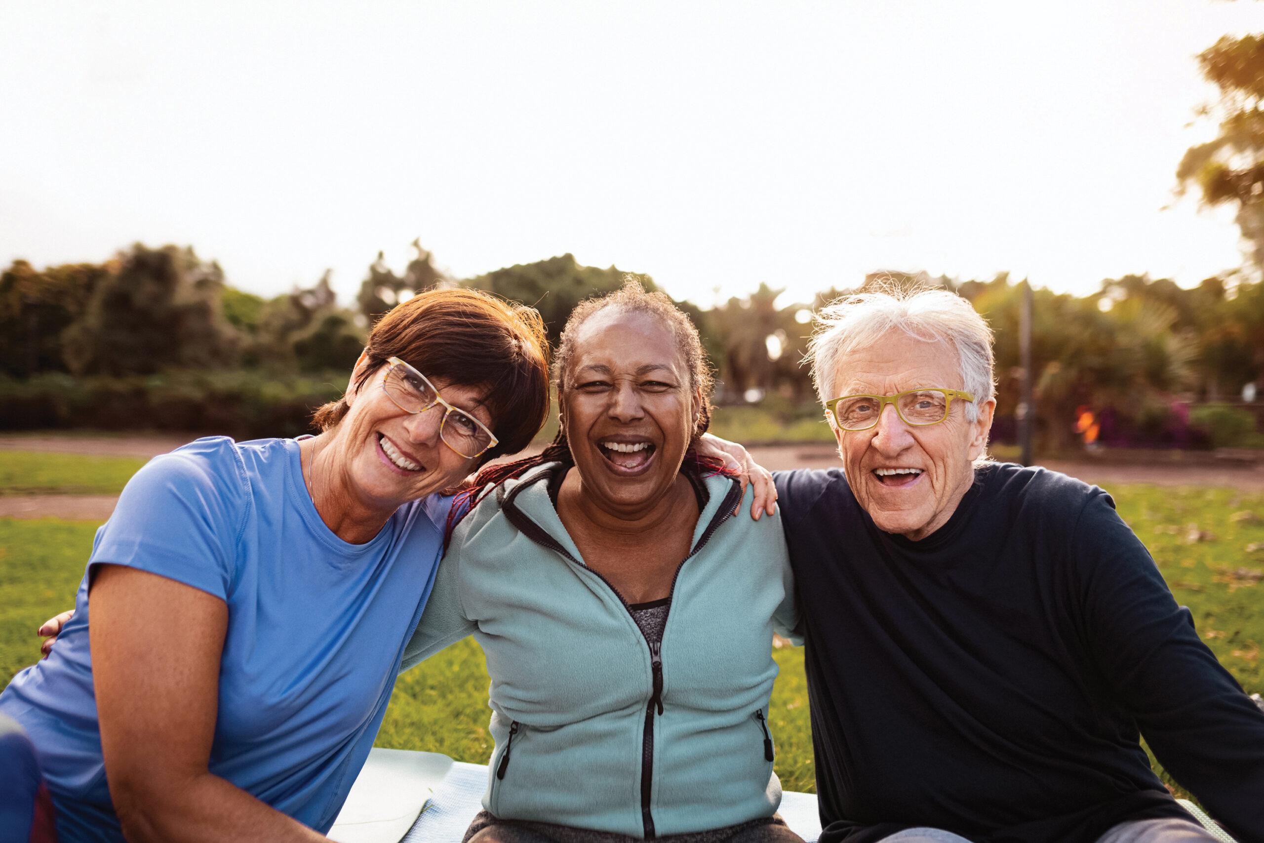 Three smiling friends sit on a blanket or mat outdoors