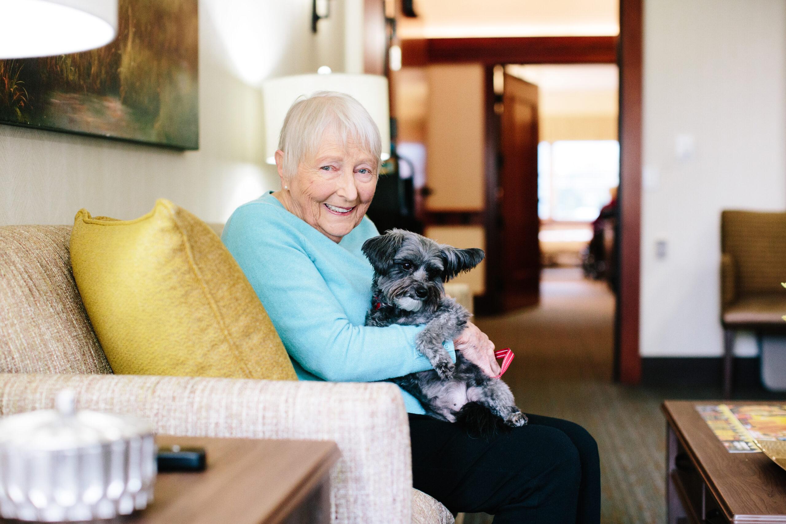 A smiling older woman holds a dog.