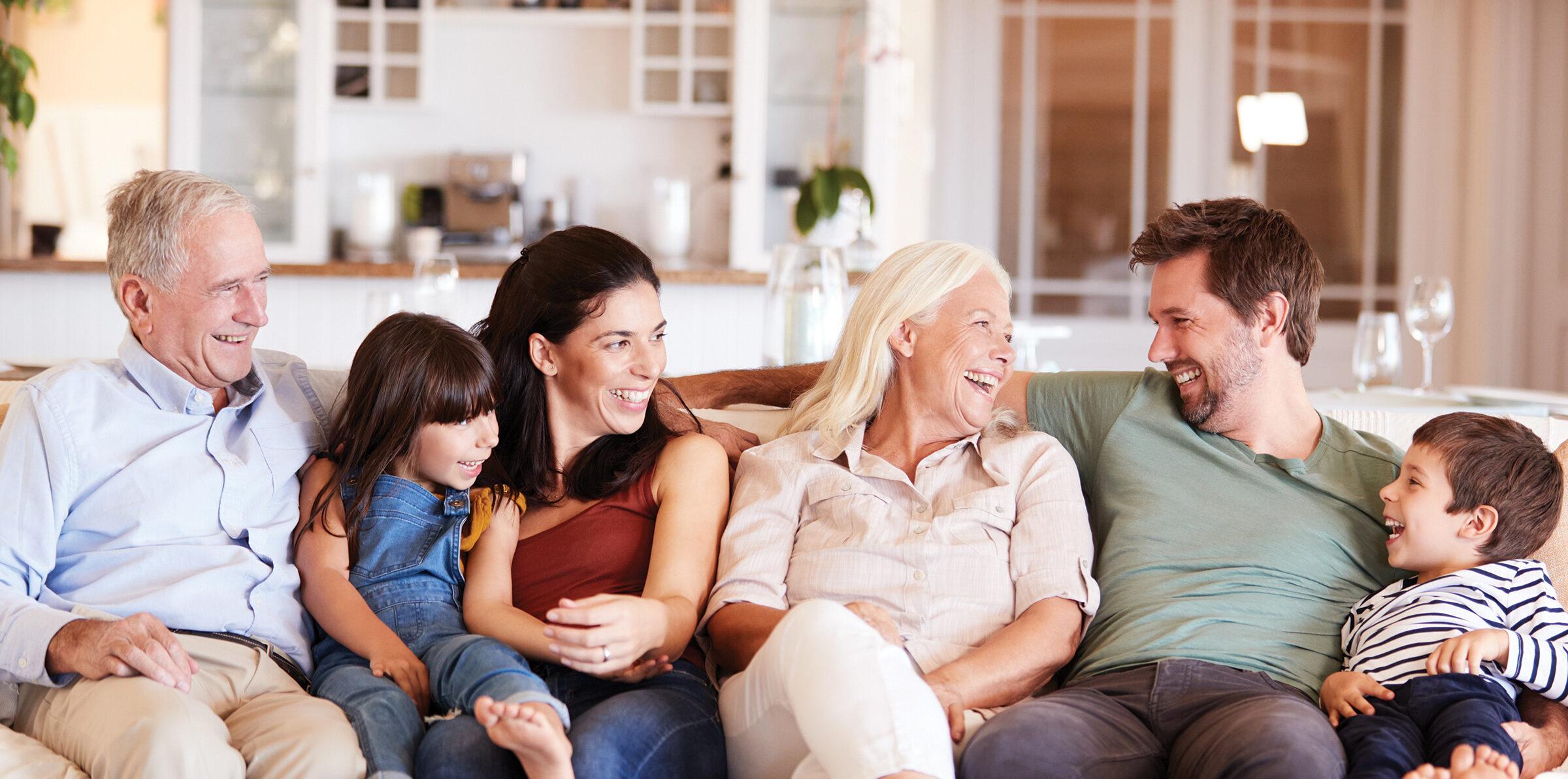 Happy three generation white family sitting on a sofa at home looking at each other, front view