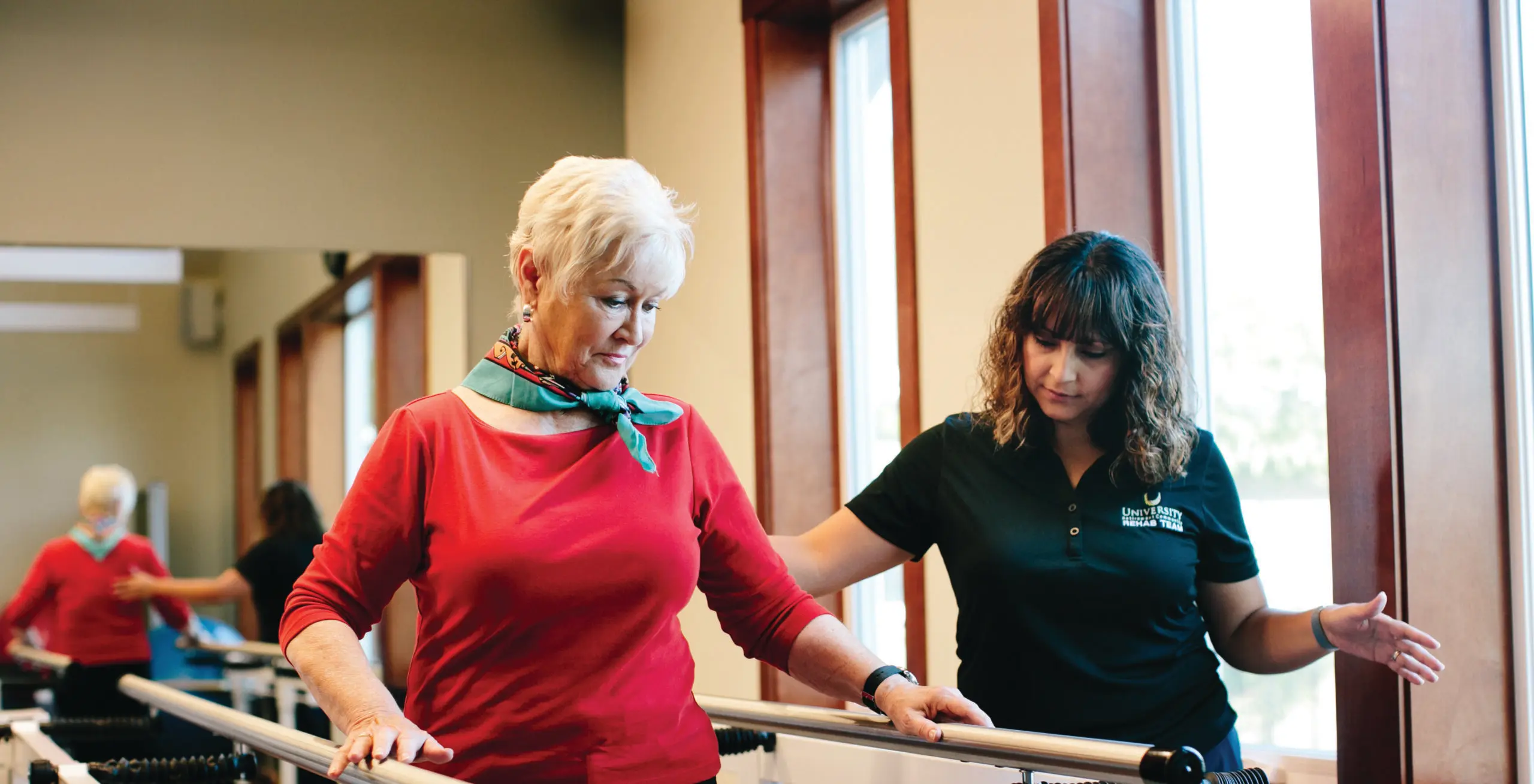 An older woman does a physical therapy exercise with a healthcare worker.